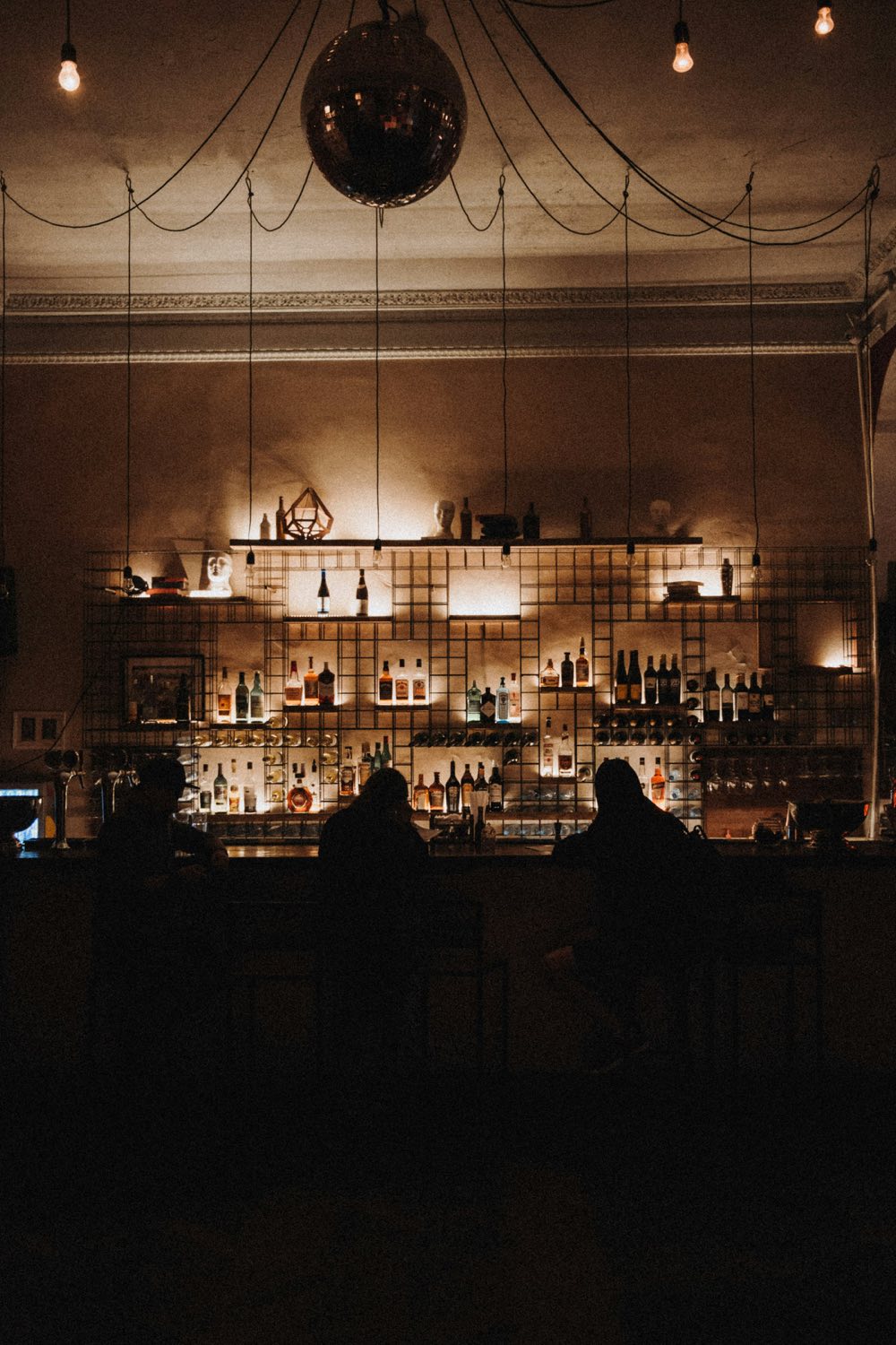 Gäste als Silhouetten an einer Bar mit Glühbirnen und Discokugel