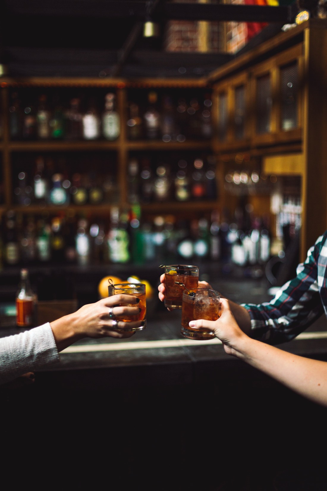 Drei Hände stossen an einer Bar mit Gläsern an